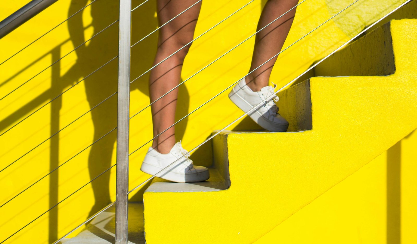 A woman wearing white shoes ascends vibrant yellow stairs in Miami. Fashion and urban style.
